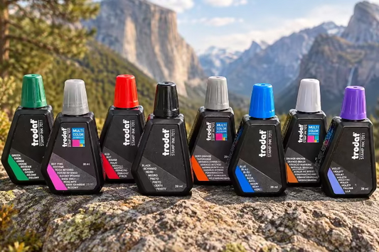 Eight small Trodat ink bottles with different colored inks on a rock in the mountains